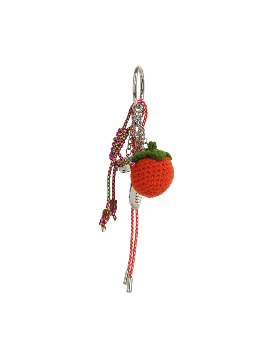 The HR Crochet Orange Keychain features a crocheted orange fruit with a green top, red and white cord, metallic accents, and a silver tassel keyring.