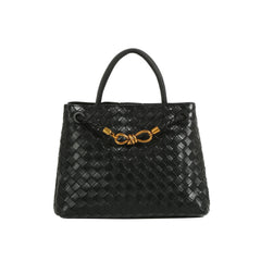 The LM Knot Accent Woven Tote is a black faux leather handbag with two handles, a gold-tone knot accent on the front, and a braided crossbody strap for versatile carrying.