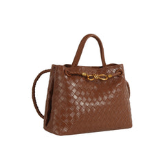 The LM Knot Accent Woven Tote is a structured brown faux leather handbag with two handles, a braided crossbody strap, and a gold-tone knot accent on the front, shown against a white background.