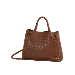 The LM Knot Accent Woven Tote is a brown faux leather handbag with two handles, a gold-tone knot accent, and a long braided crossbody strap, shown against a white background.