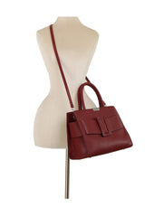 The LM Buckle Accented Structured Tote features burgundy leather, a top handle, detachable crossbody strap, and a front flap with an oversized bow, showcased on a cream mannequin torso.