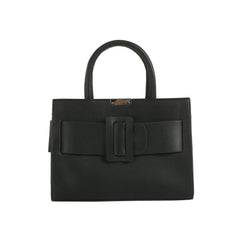 The LM Buckle Accented Structured Tote is a black leather bag with two handles, a bold decorative buckle, front bow detail, and a detachable crossbody strap for versatile styling.